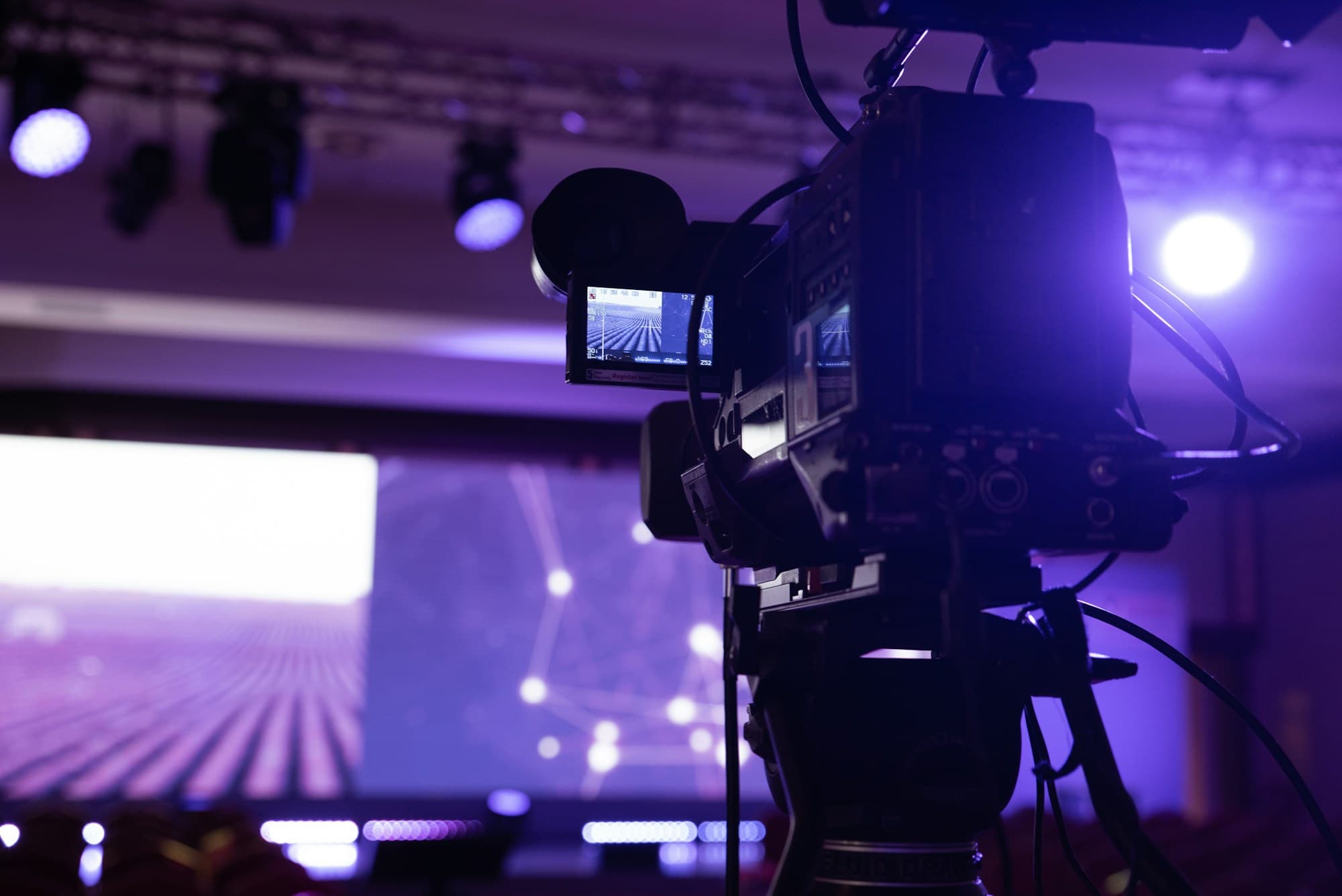 A broadcast camera on a tripod captures a stage during a live event