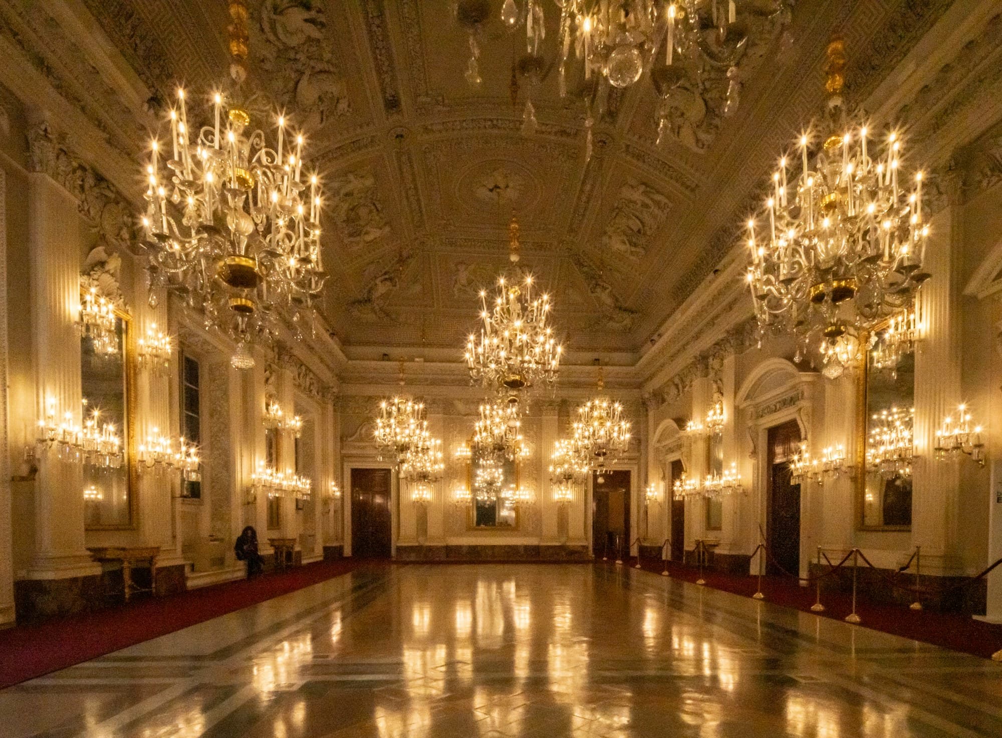 A grand ballroom set for a gala evening beneath ornate chandeliers